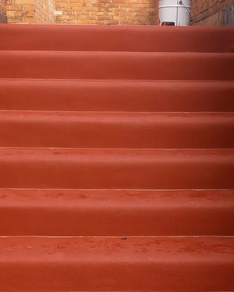Scala esterna tra muri di mattoni, con gradini in gomma rossa