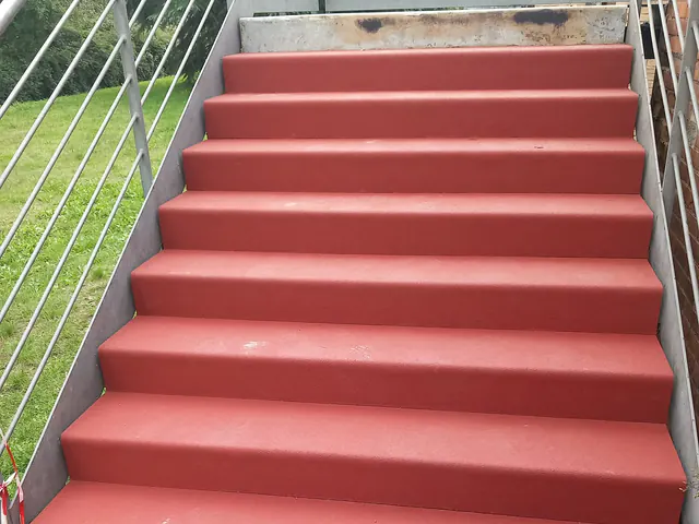 Scala esterna accanto a un prato, con gradini in gomma rossa