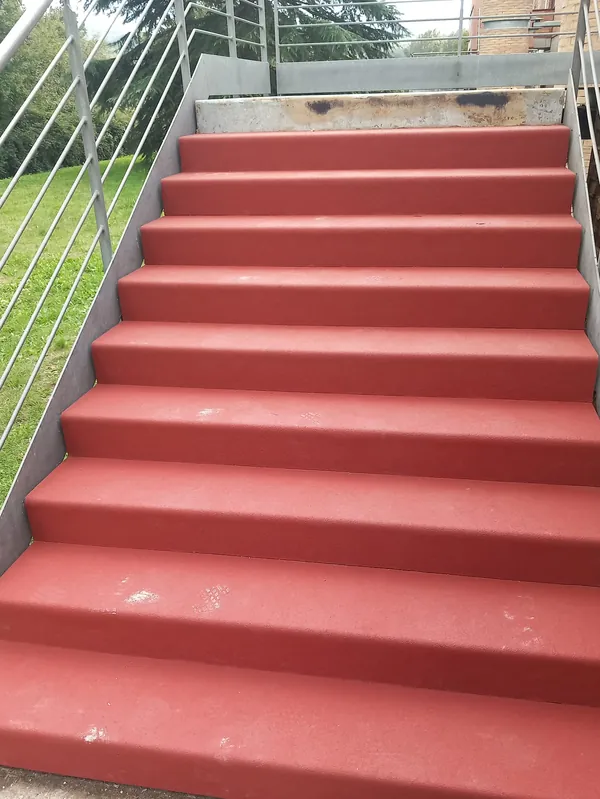 Scala esterna accanto a un prato, con gradini in gomma rossa